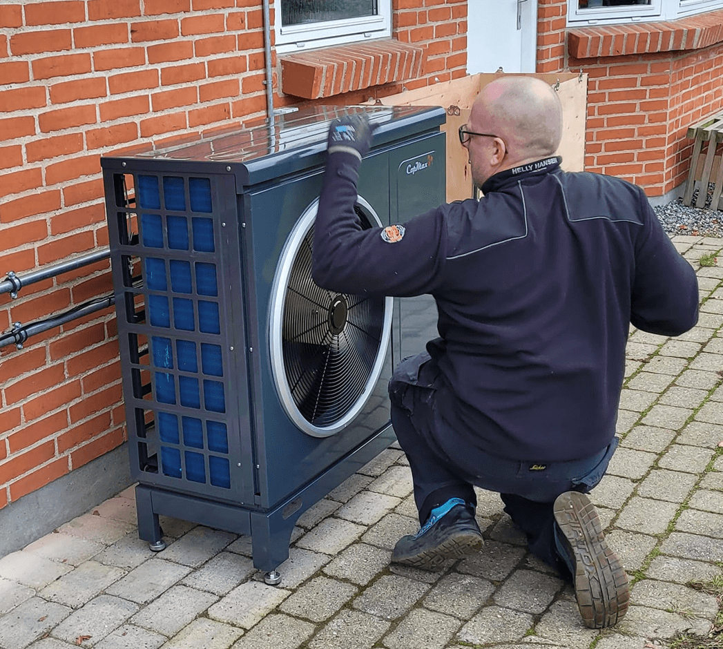 Tekniker servicerer en luft-til-vand varmepumpe ved en murstensvilla